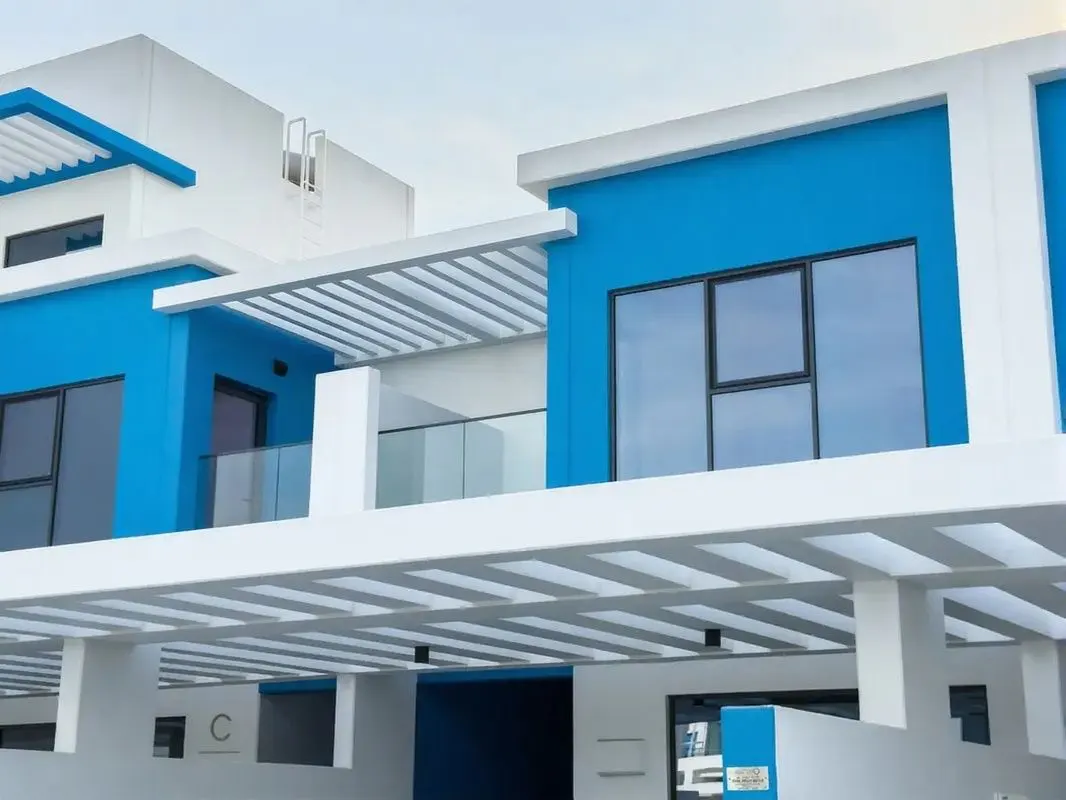 Exterior view of modern two-story homes with blue walls, white trim, and large windows under a bright sky.