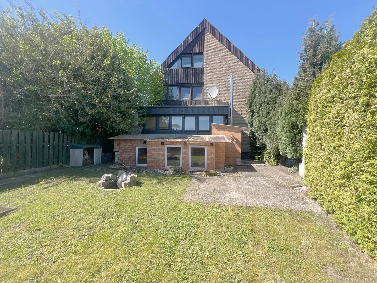 A two-story house with a brick extension and a green lawn on a sunny day.