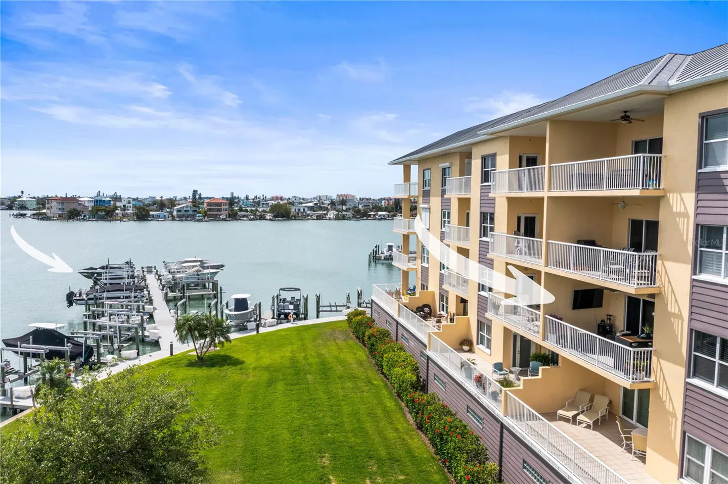 Waterfront condo with balconies overlooking a boat dock on a sunny day. The building is tan with white railings and a gray roof.
