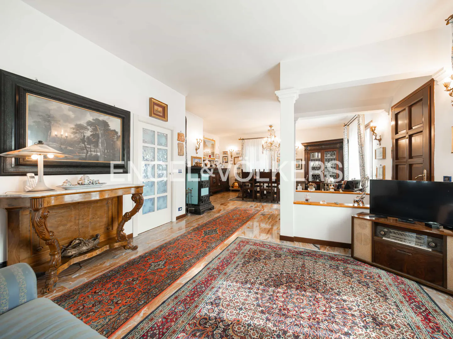 A spacious living room with a large rug, wooden console table, and a framed landscape painting.