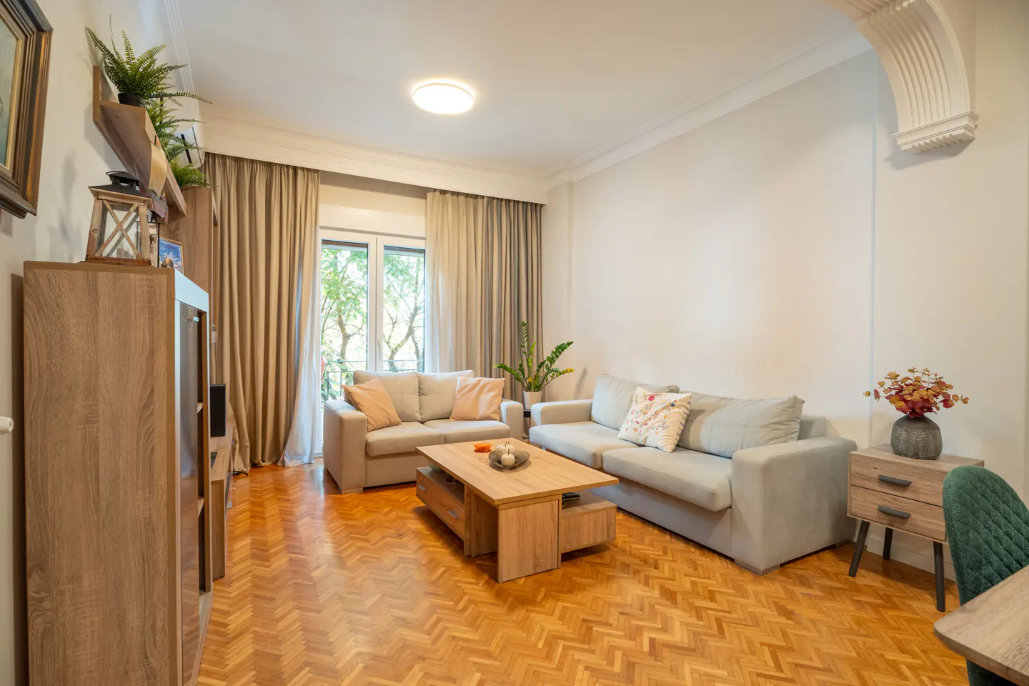 Living room with wood floors, two sofas, and a wood coffee table. A window with curtains is in the background.