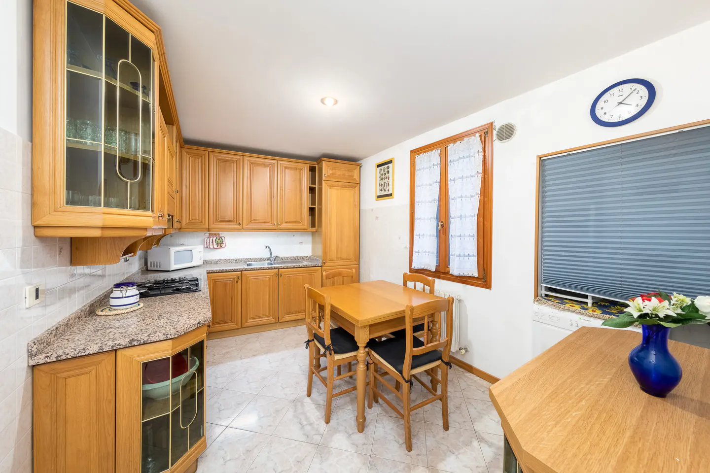 A bright kitchen with wooden cabinets, a table with four chairs, and a blue vase with white flowers.