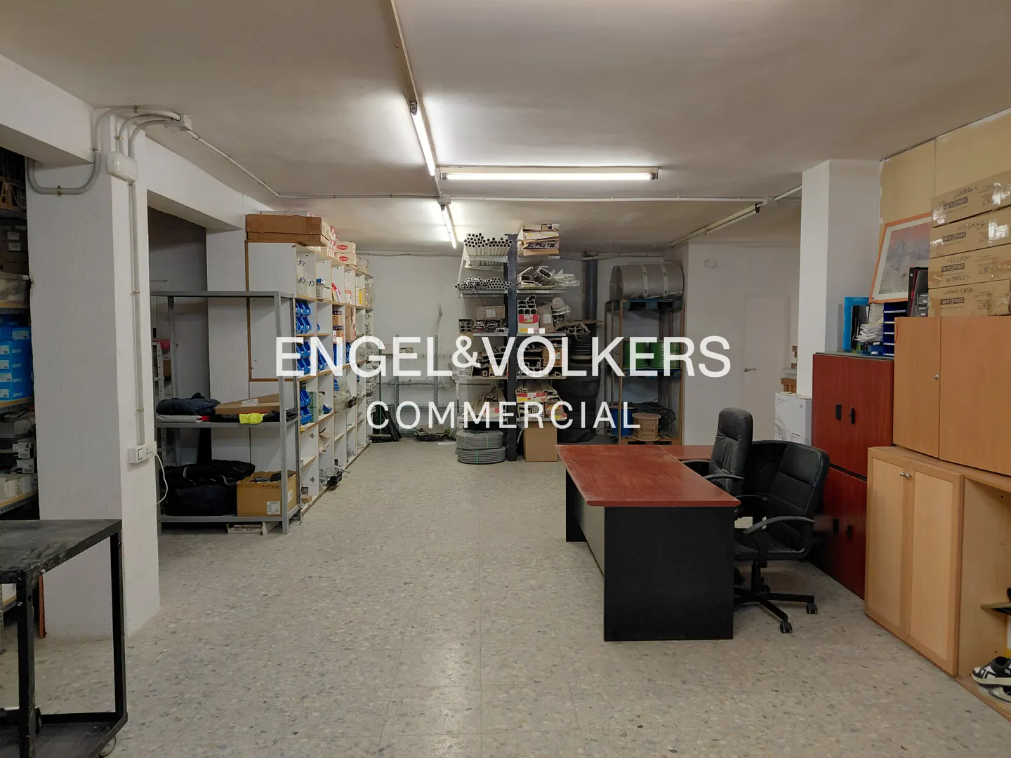 A commercial space with shelves stocked with items, a desk, and office chairs.