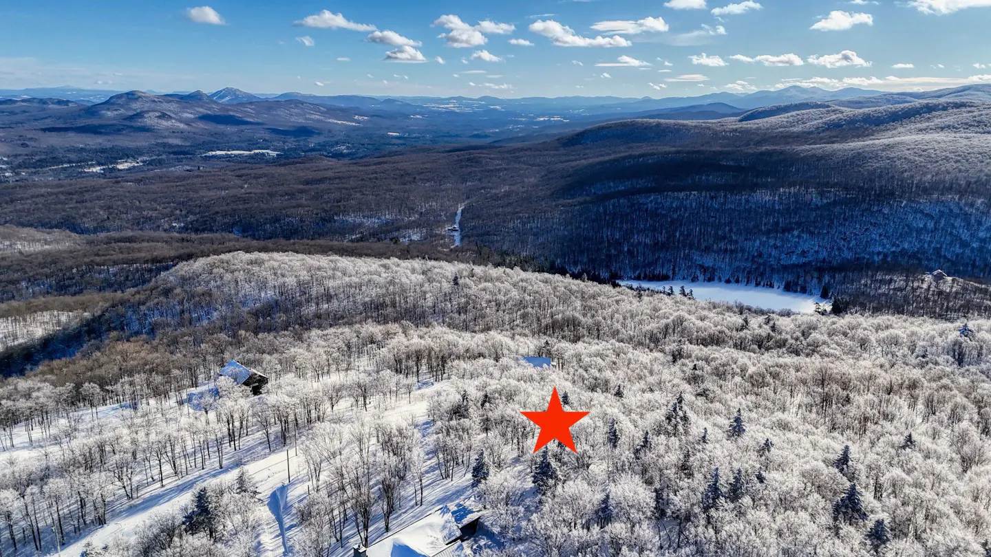 Aerial view of a snow-covered mountain landscape with a red star marking a property location. Distant mountains and a blue sky are visible.