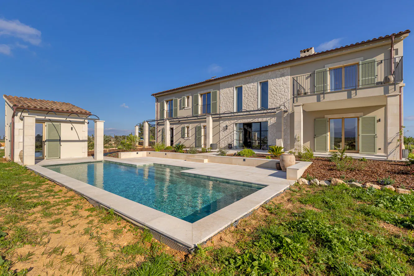Two-story house with a pool. The house is beige with green shutters and a red tile roof. The pool is turquoise and surrounded by a white stone patio.