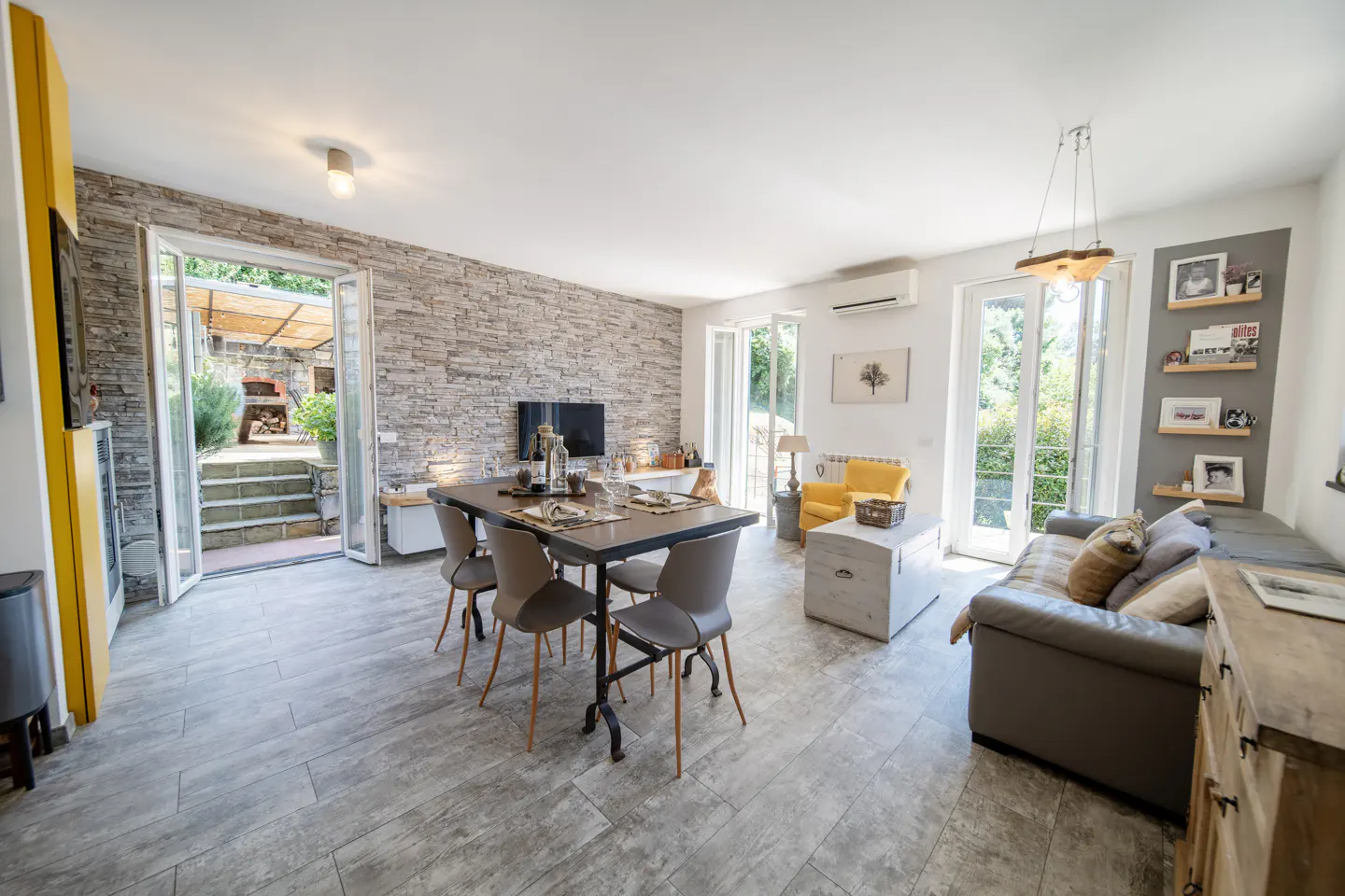 Bright living room with stone accent wall, dining table, gray sofa, and open doors to an outdoor patio.