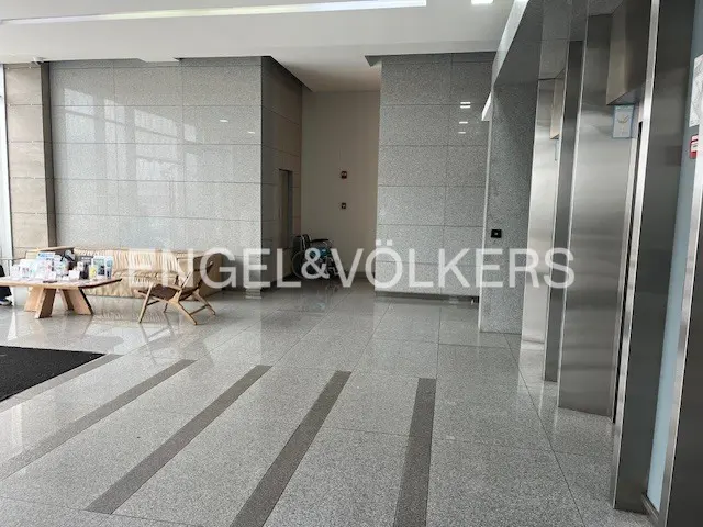 Lobby with gray granite walls, floor, and stainless steel elevators. A table, chairs, and sofa are in the background.