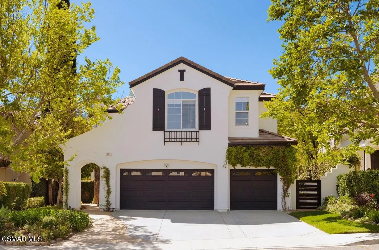 Two-story white house with brown trim, black shutters, and a two-car garage under a clear blue sky.