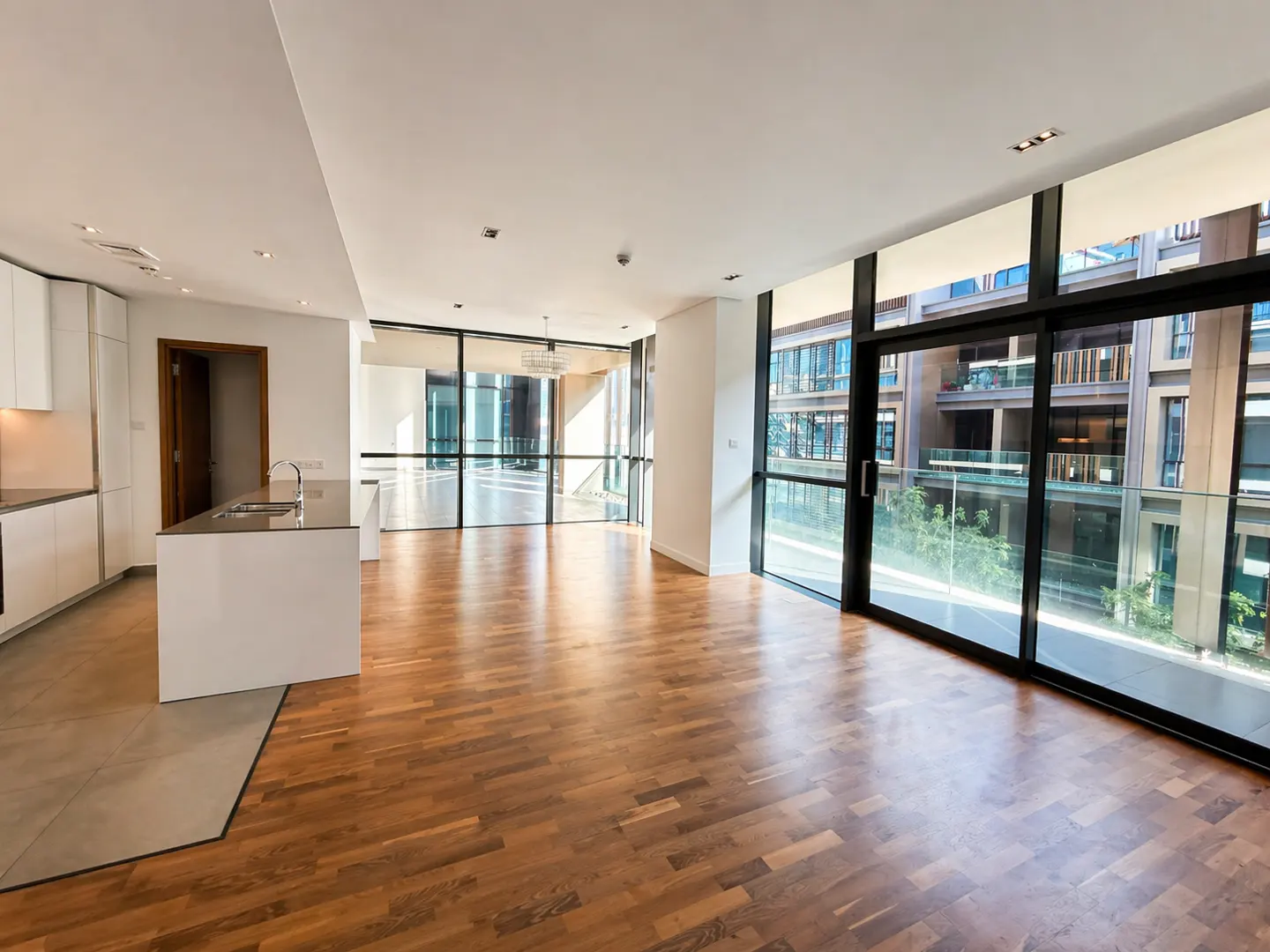 Bright, modern apartment with wood floors, white kitchen, and large windows overlooking a building.