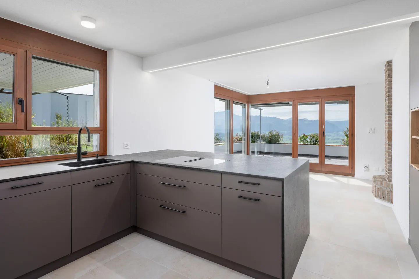 A modern kitchen with gray cabinets, a black sink, and wood-framed windows overlooking a mountain view.