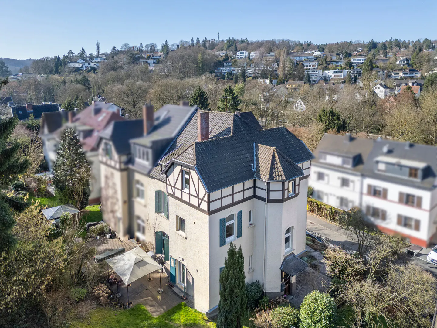 Aerial view of a cream-colored, half-timbered house with a dark gray roof, green shutters, and a garden with a white canopy.