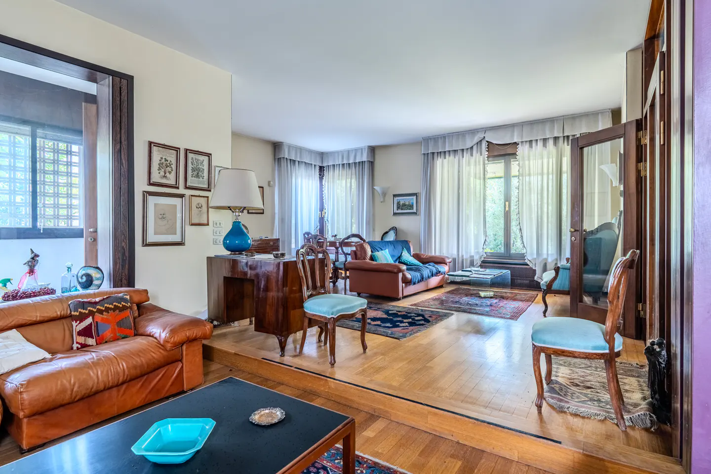 Spacious living room with a sunken seating area, leather sofas, wooden furniture, and light blue upholstered chairs.
