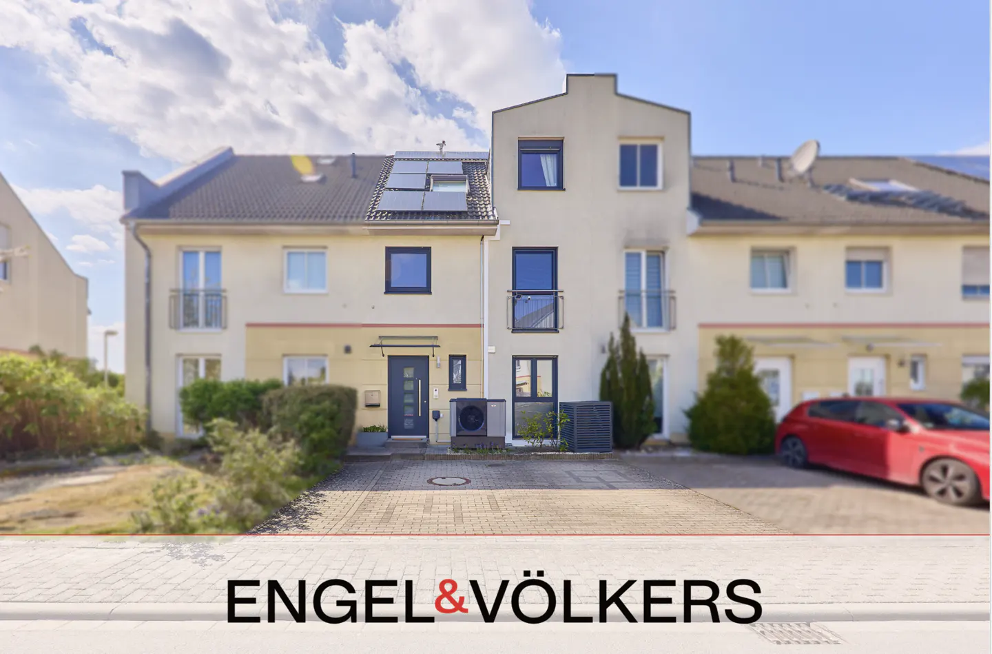 Exterior view of modern townhouses with solar panels, a red car parked in front, and the Engel & Völkers logo.