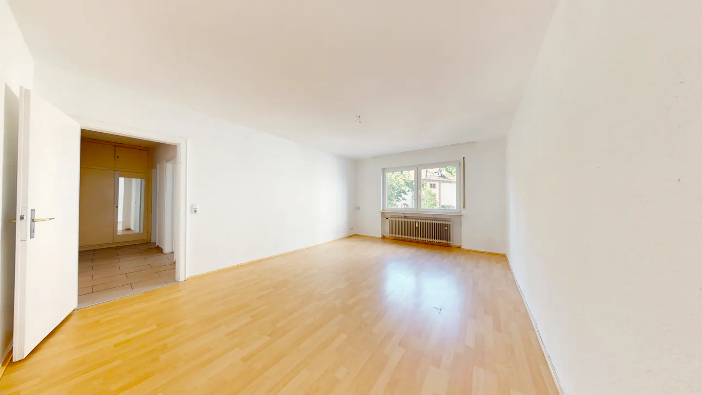 Bright, empty room with wood floors, white walls, and a window. An open door reveals a closet with a mirror.