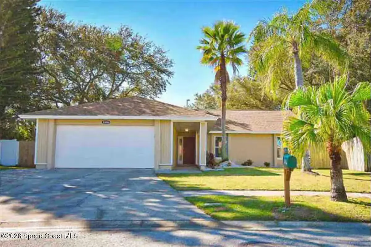 Beige single-story home with a white garage door, palm trees, and a green mailbox on a sunny day.