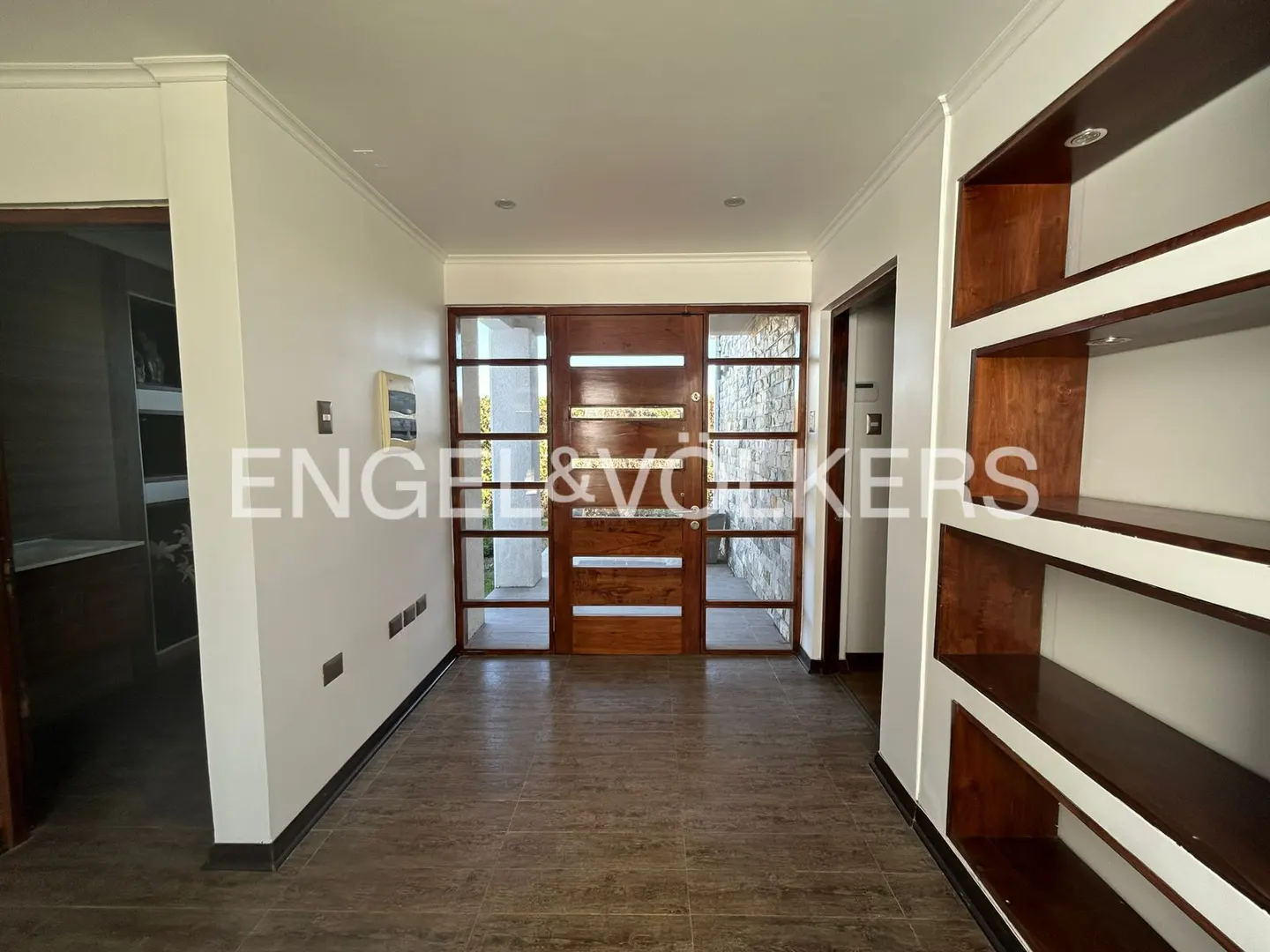 A home's entryway features a wood door with glass panels, white walls, and built-in shelves.