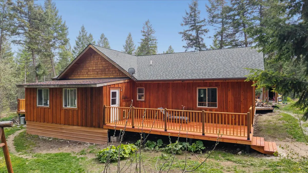 Exterior view of a wood cabin with a deck, surrounded by green trees and grass under a blue sky.