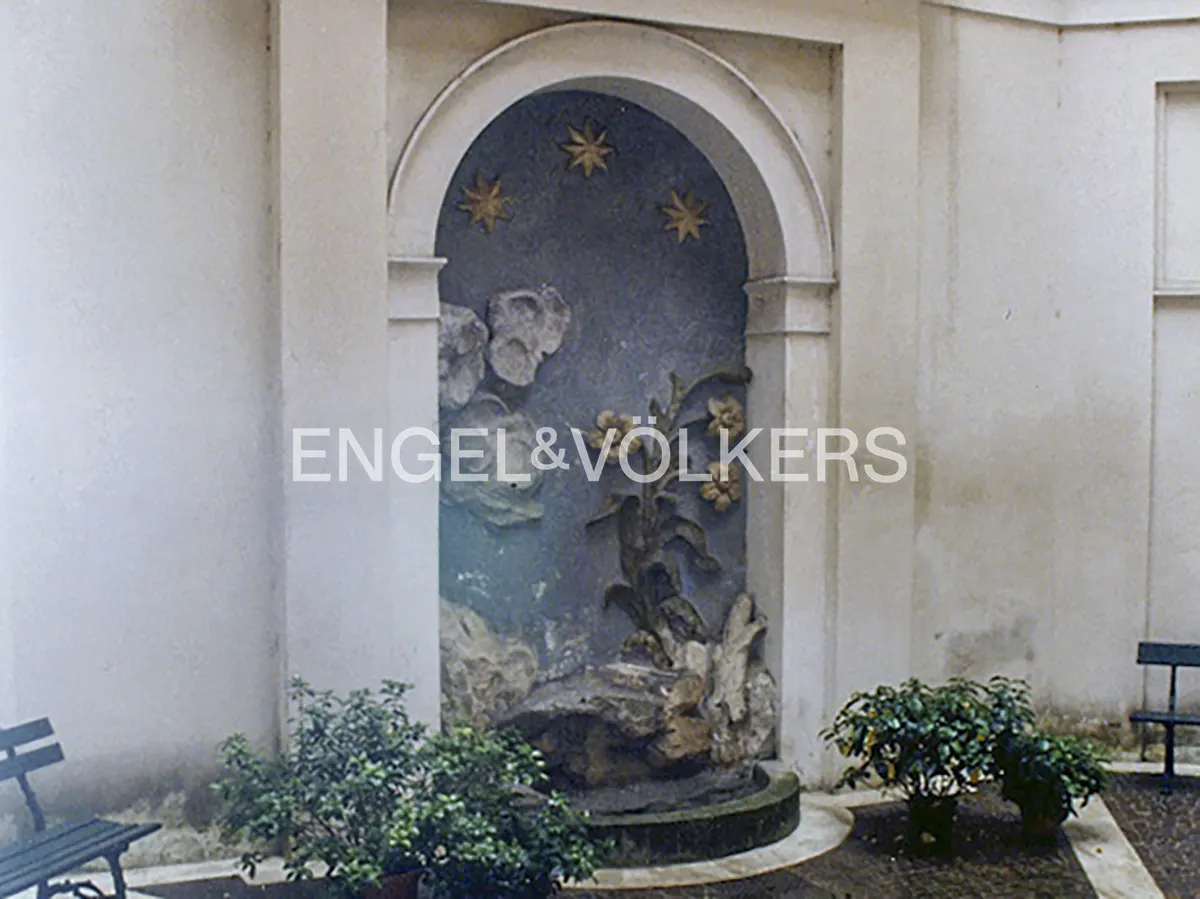 An arched stone wall niche features a blue background with gold stars, floral reliefs, and a small fountain basin.