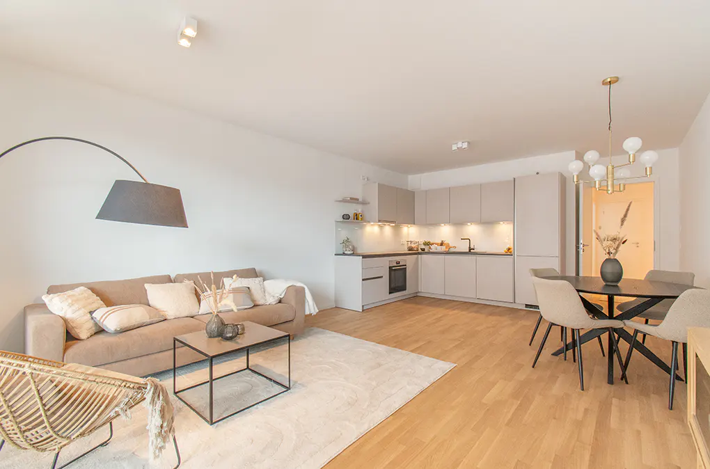 Open-plan living area with a beige sofa, modern kitchen, and dining table with chairs on light wood floors.