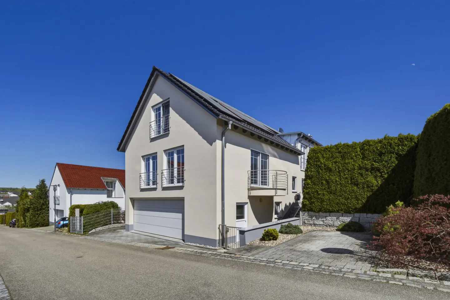Two-story beige house with a gray roof, garage, and small balconies under a clear blue sky.
