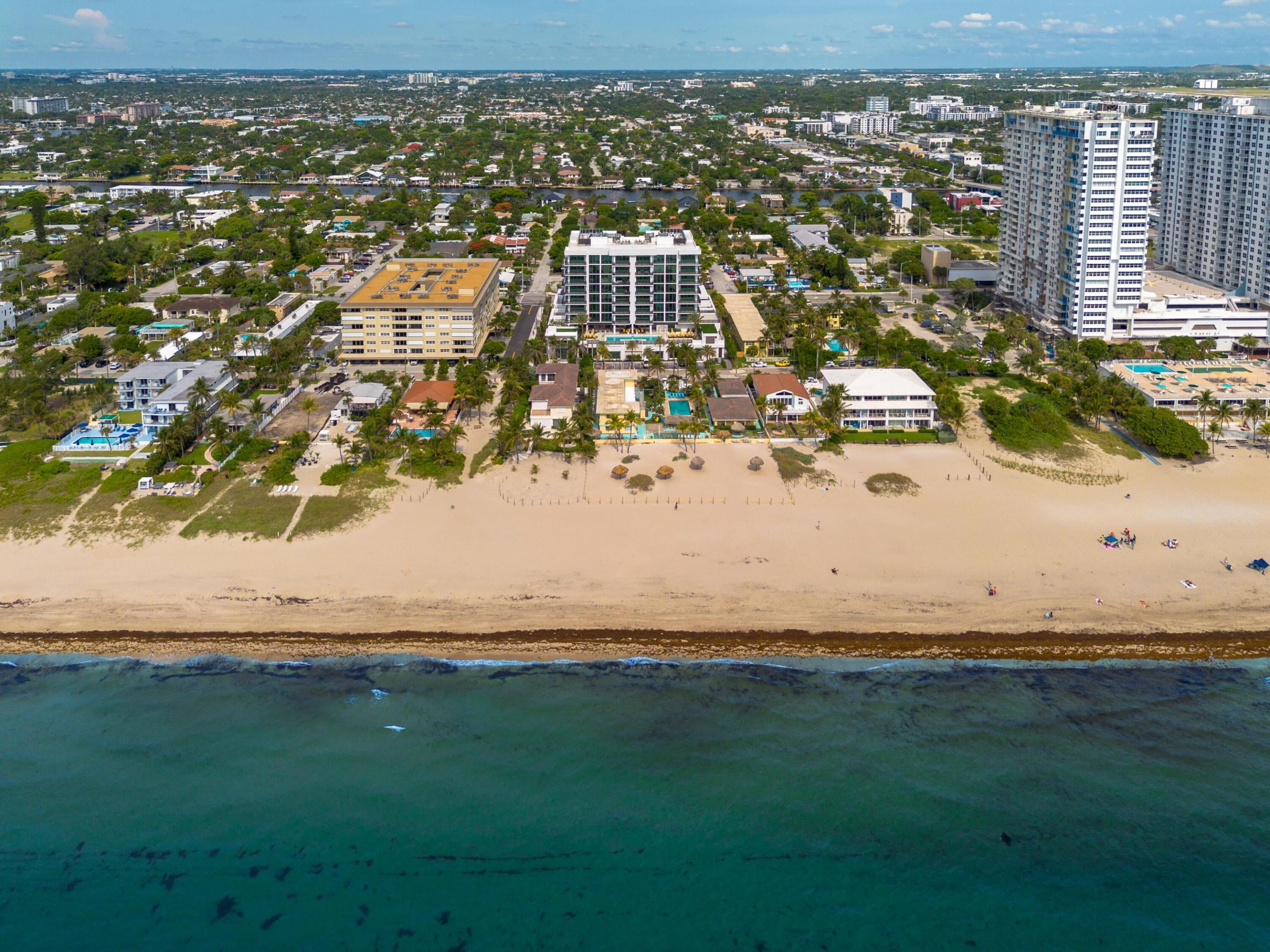 Aerial view of a sandy beach with turquoise ocean water, beachfront hotels, and a sprawling coastal city in the background. [AI-generated text]