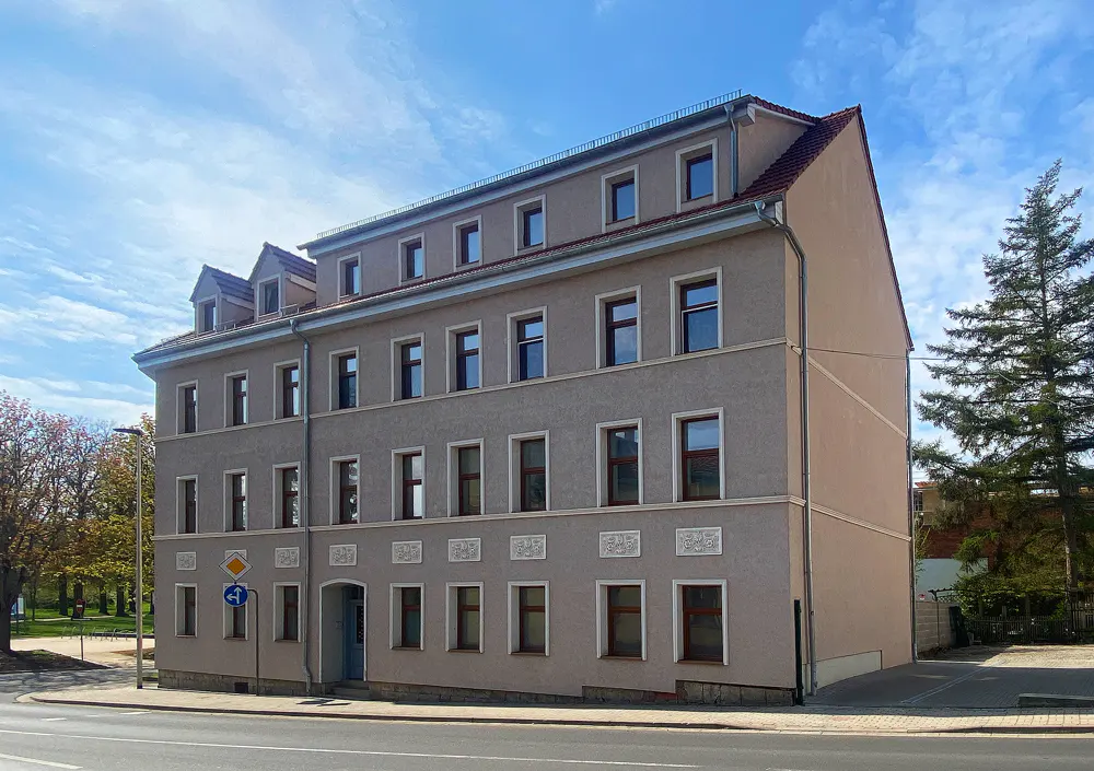 Three-story apartment building with a red roof and many windows under a blue sky.