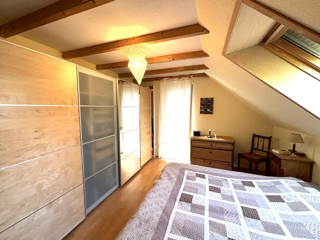 Attic bedroom with a patchwork quilt, wooden beams, and built-in wardrobes. A window lets in natural light.