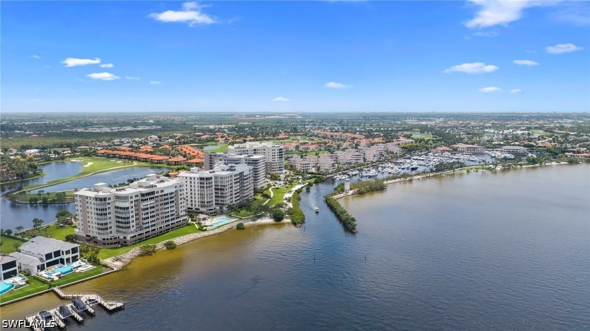 Aerial view of waterfront condos, a marina filled with boats, and a golf course under a blue sky.