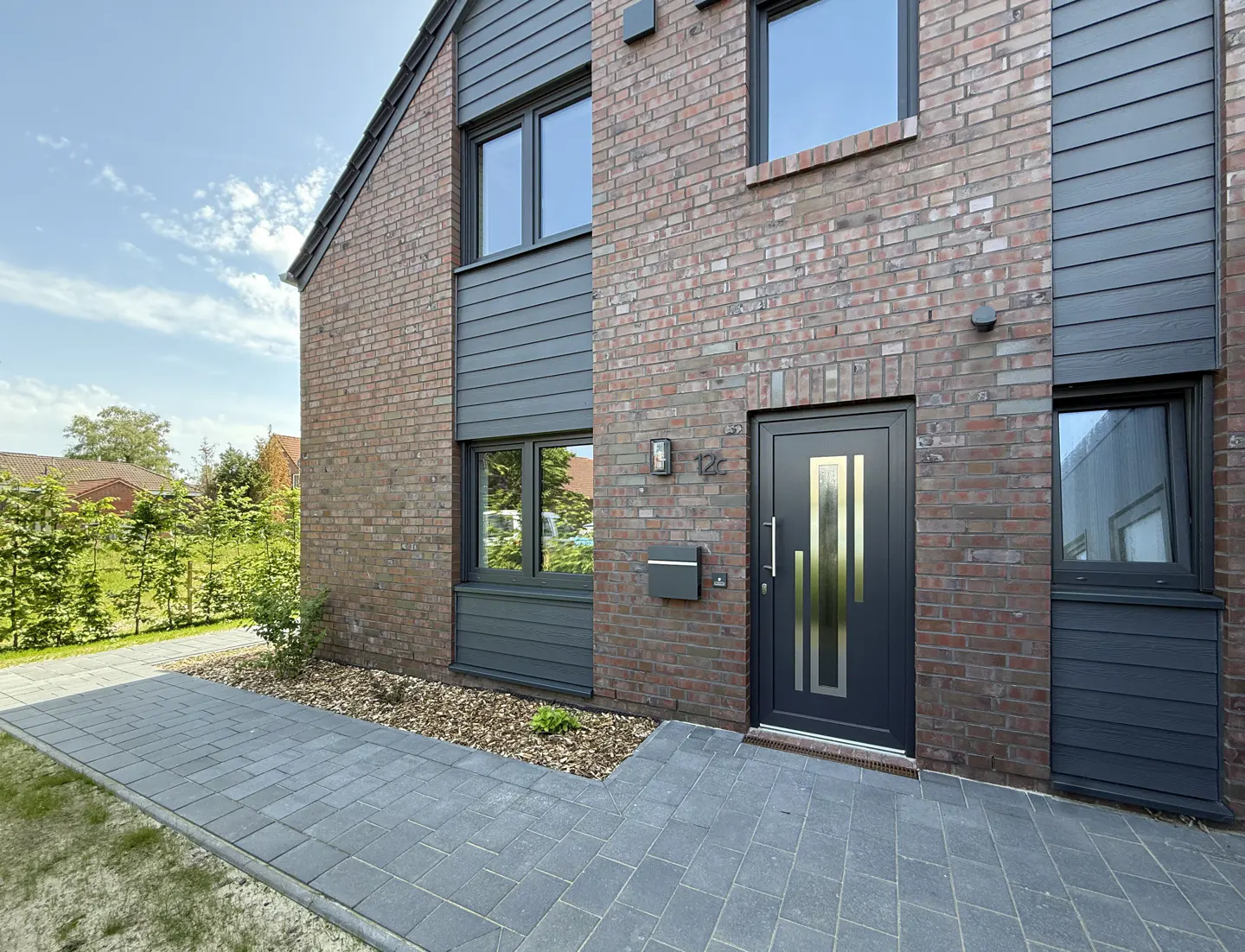 Exterior view of a two-story house with brick and gray siding, a gray front door with gold accents, and a gray brick walkway.