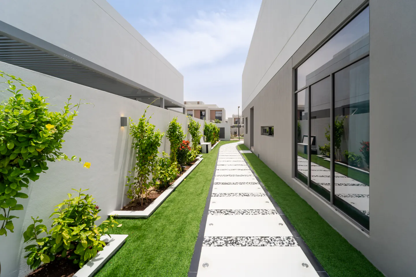 Modern home exterior with a stone walkway, green grass, and white walls. Plants line the walkway.
