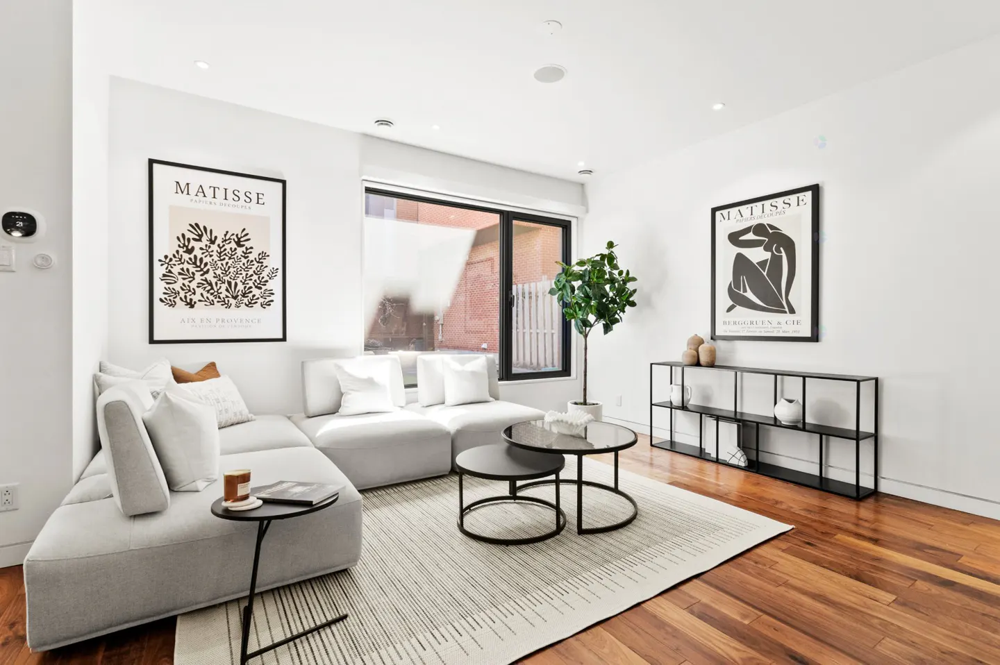 Modern living room with a light gray sectional sofa, two round coffee tables, a potted plant, and Matisse wall art.