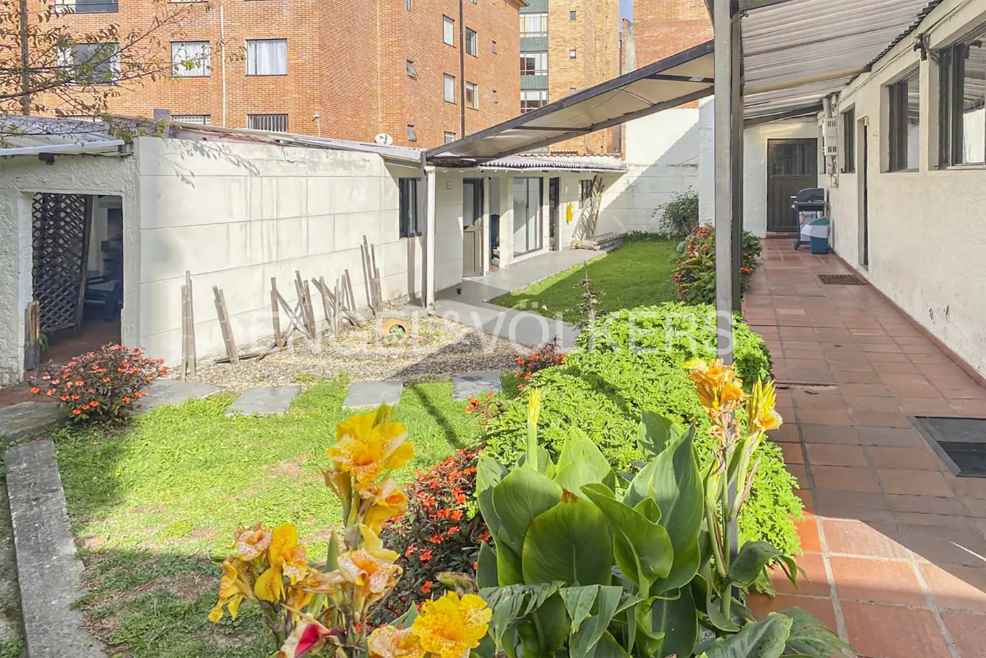 Exterior view of a white building with a garden, flowers, and a brick walkway.