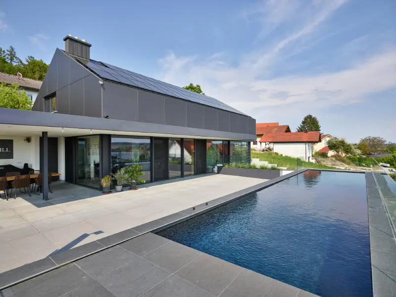 Modern gray house with solar panels and a dark blue pool on a sunny day.