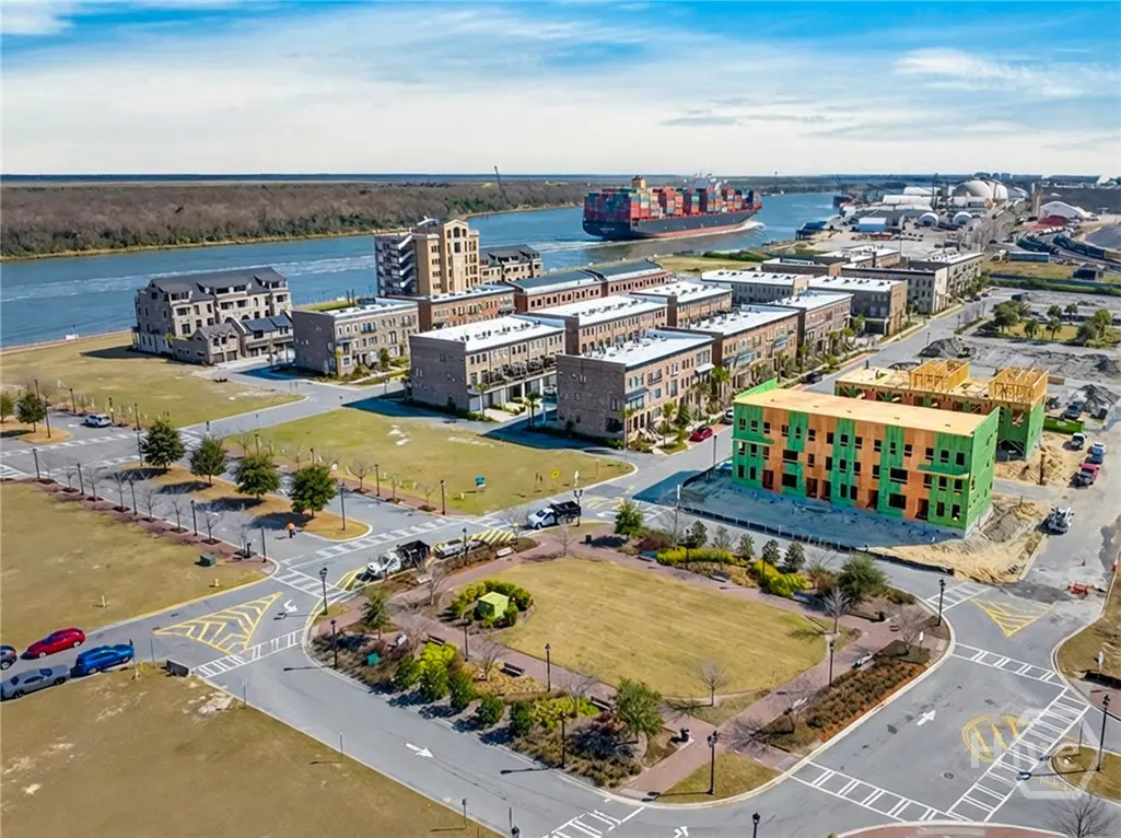 Aerial view of a waterfront neighborhood with brick townhouses, a green park, and a cargo ship on the river.