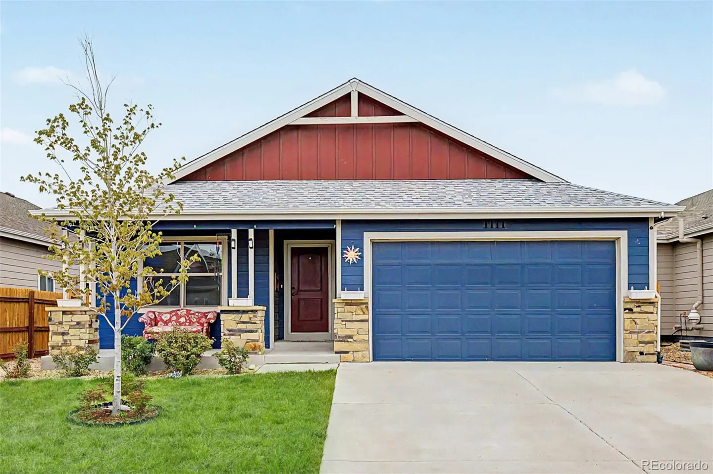 A blue house with a red gable and a gray roof. A tree stands in the front yard.