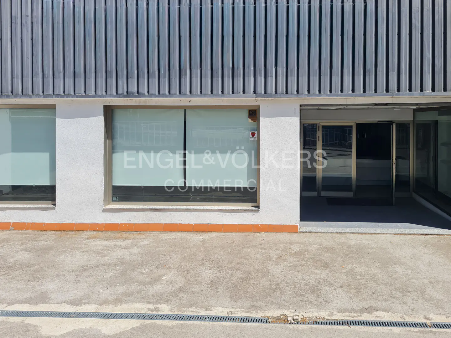 Exterior view of a commercial building with white walls, large glass windows, and a metal-paneled upper facade.