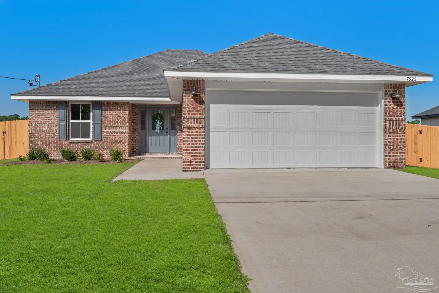 A single-story brick house with a gray roof, white garage door, and green lawn under a blue sky.