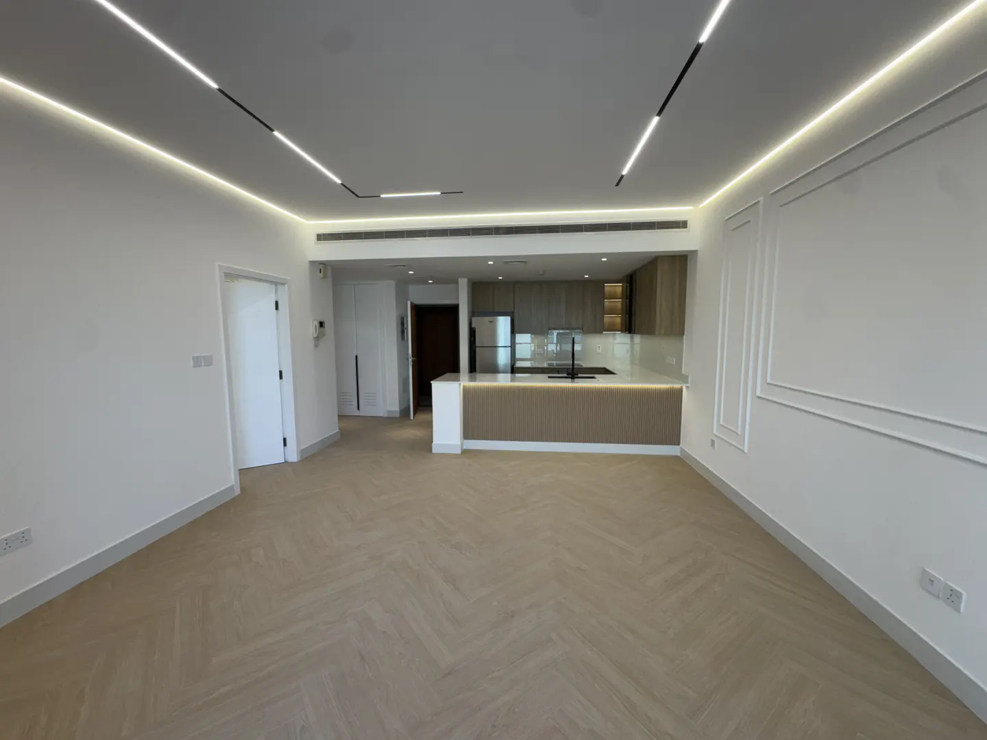 Bright, modern apartment interior with herringbone wood floors, white walls, and an open kitchen with wood cabinets.