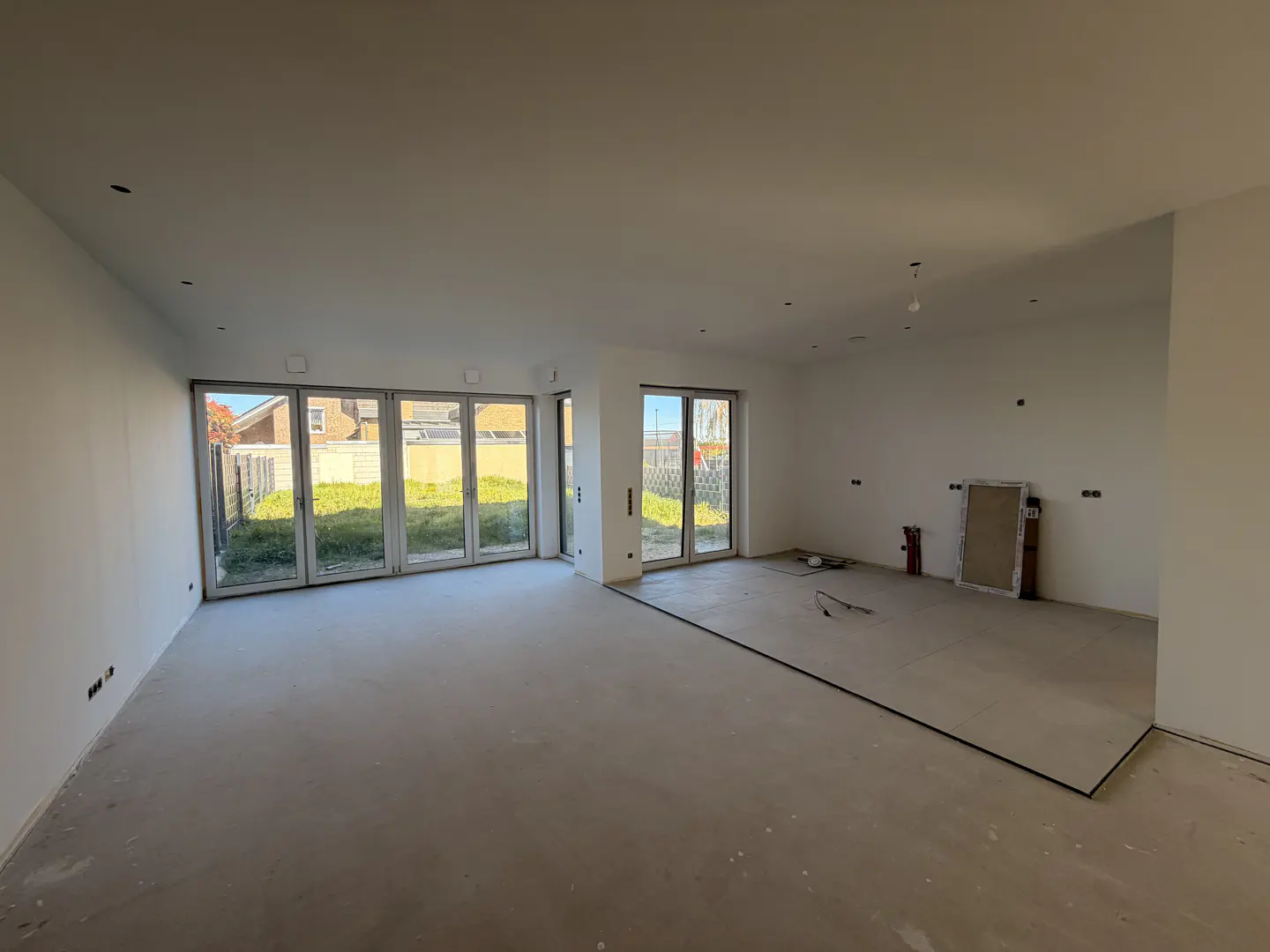Unfinished living room with white walls, concrete floor, and large glass doors leading to a green yard.