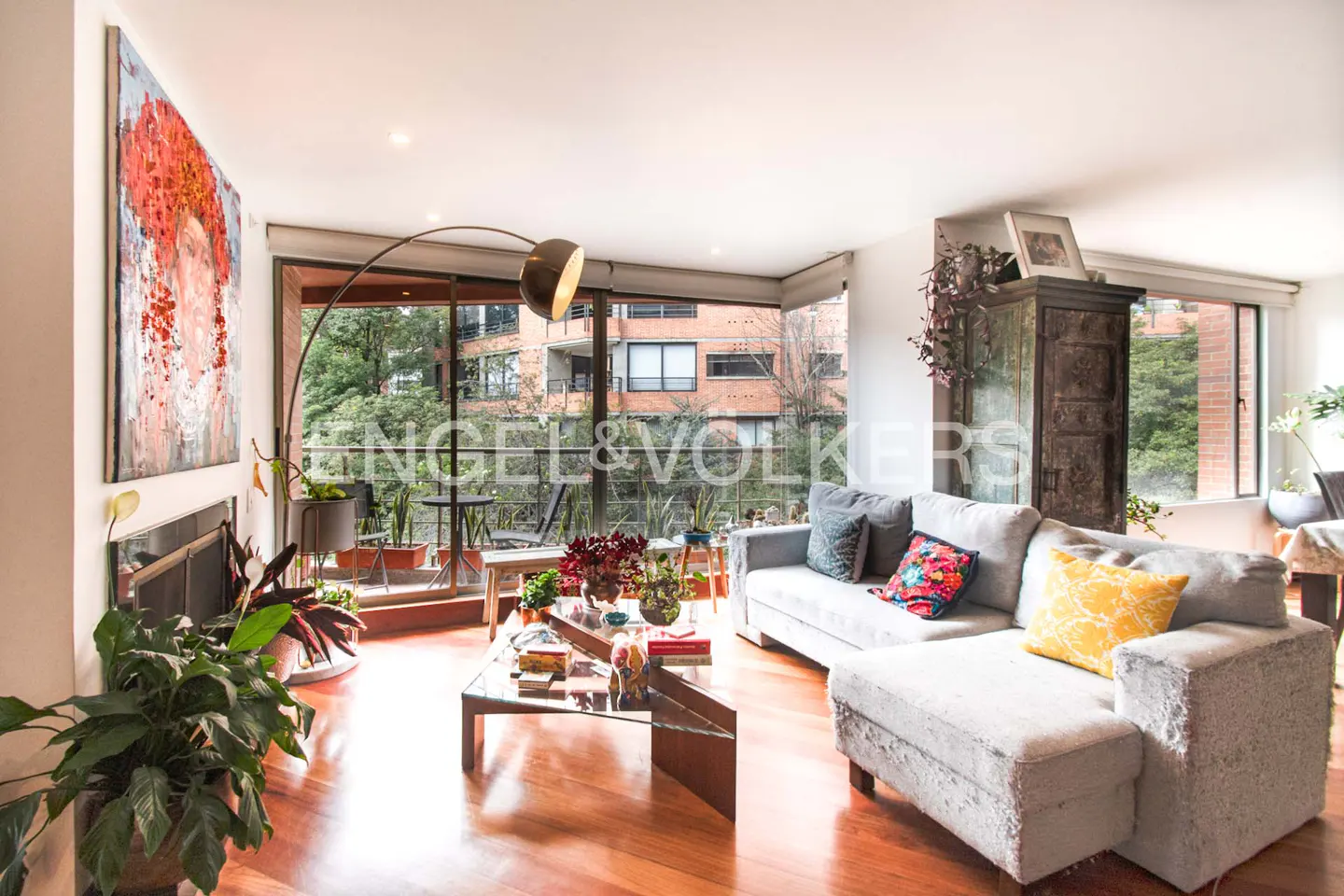 Bright living room with hardwood floors, a grey sectional sofa, a glass coffee table, and a large abstract red painting.