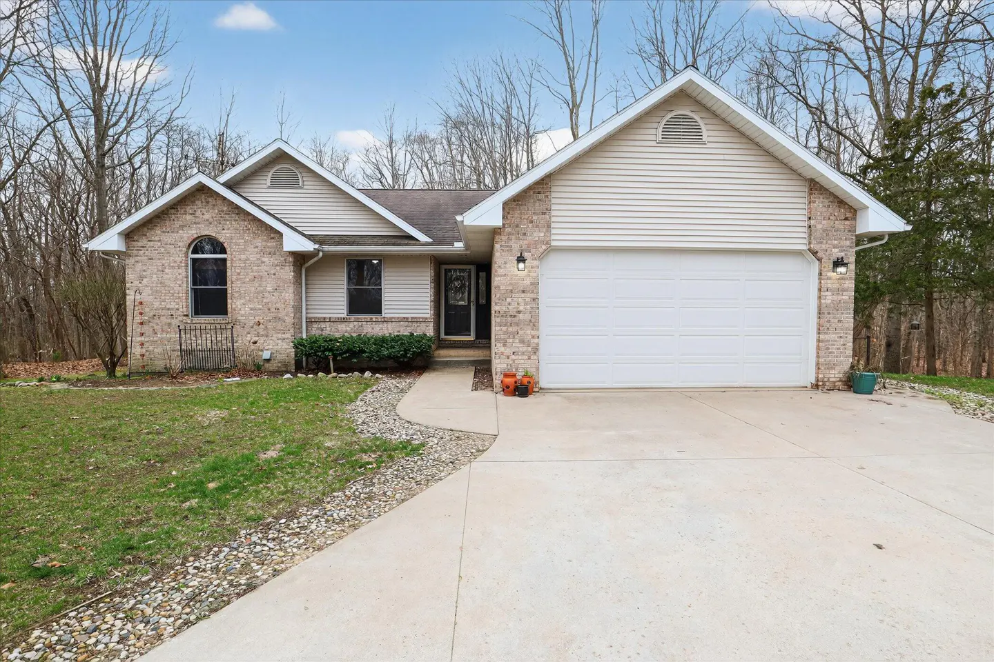 Beige brick and vinyl siding house with a white garage door and concrete driveway on a sunny day.