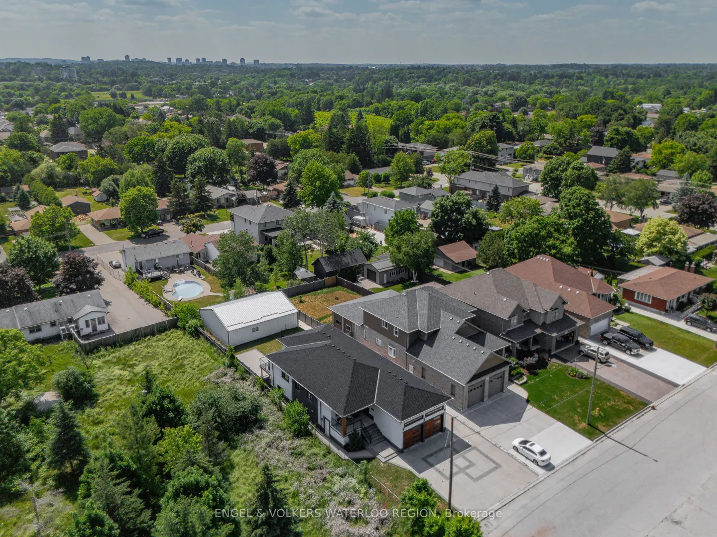 Aerial view of a suburban neighborhood with houses, green trees, and a city skyline in the distance.