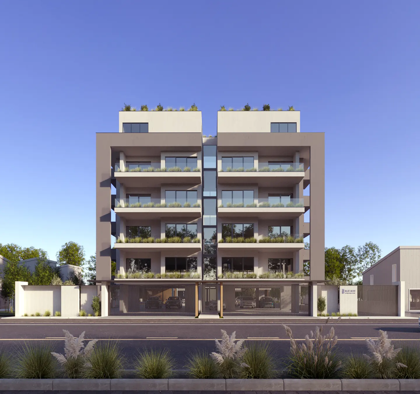 Modern four-story apartment building with balconies, gray facade, and gated parking. Blue sky background.