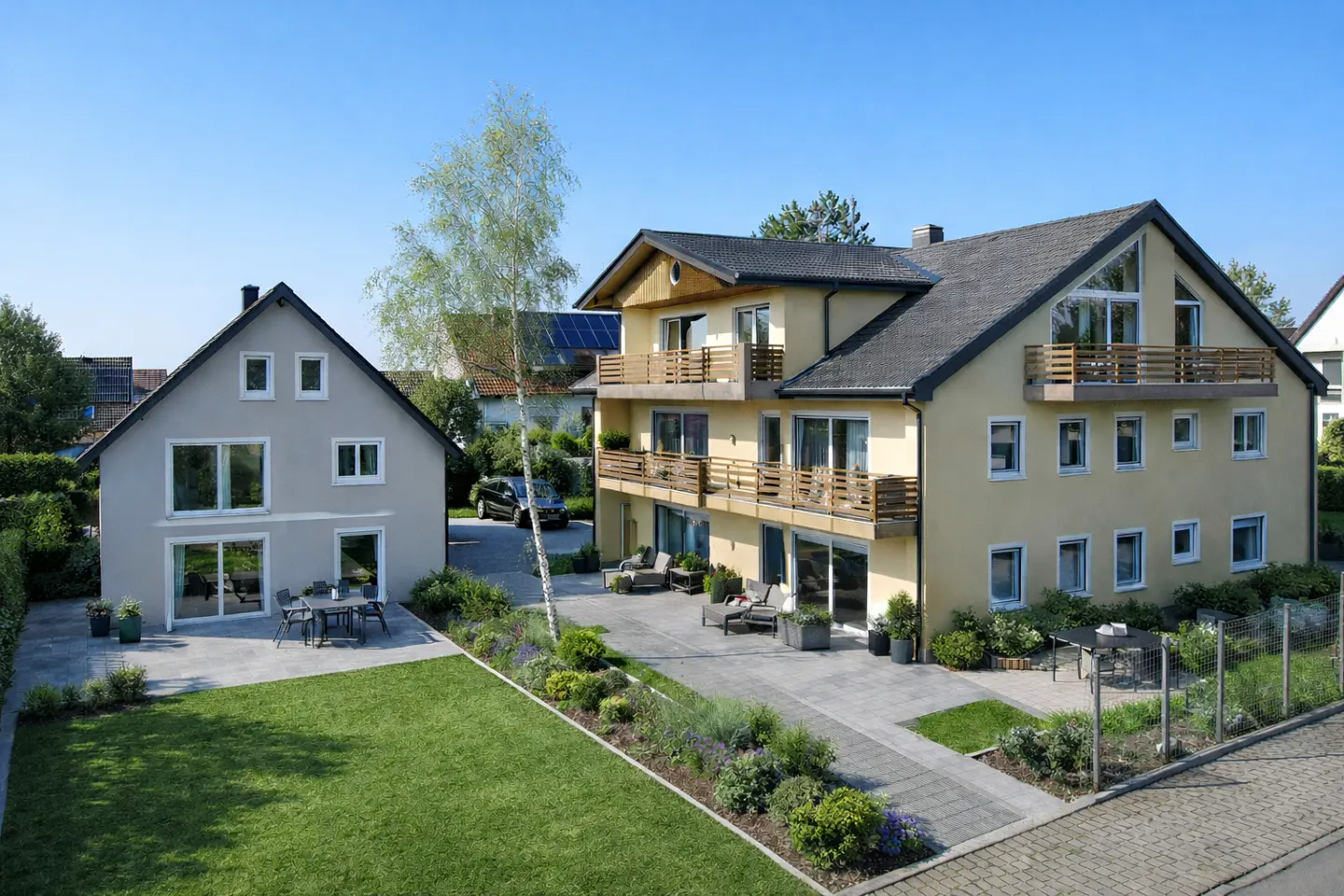 Two-story yellow house with balconies and a gray house with a green lawn on a sunny day.