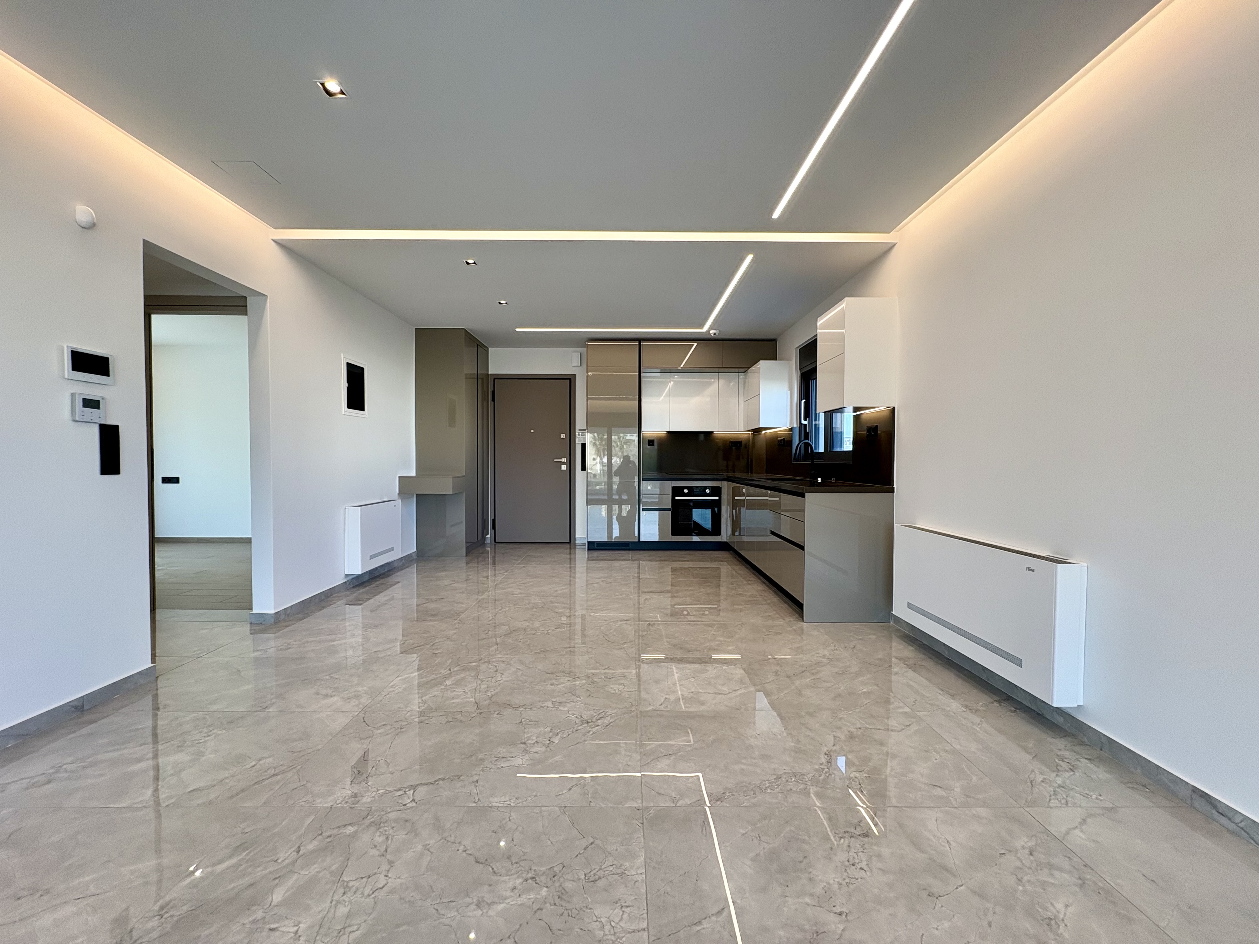 A modern, empty apartment with gray marble floors, white walls, and a sleek kitchen with white and gray cabinets.