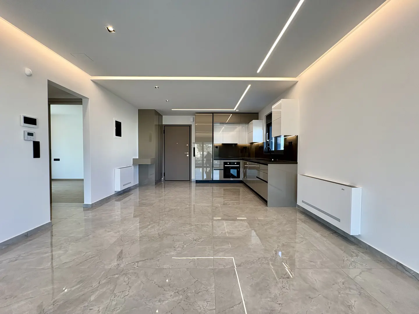 A modern, empty apartment with gray marble floors, white walls, and a sleek kitchen with white and gray cabinets.