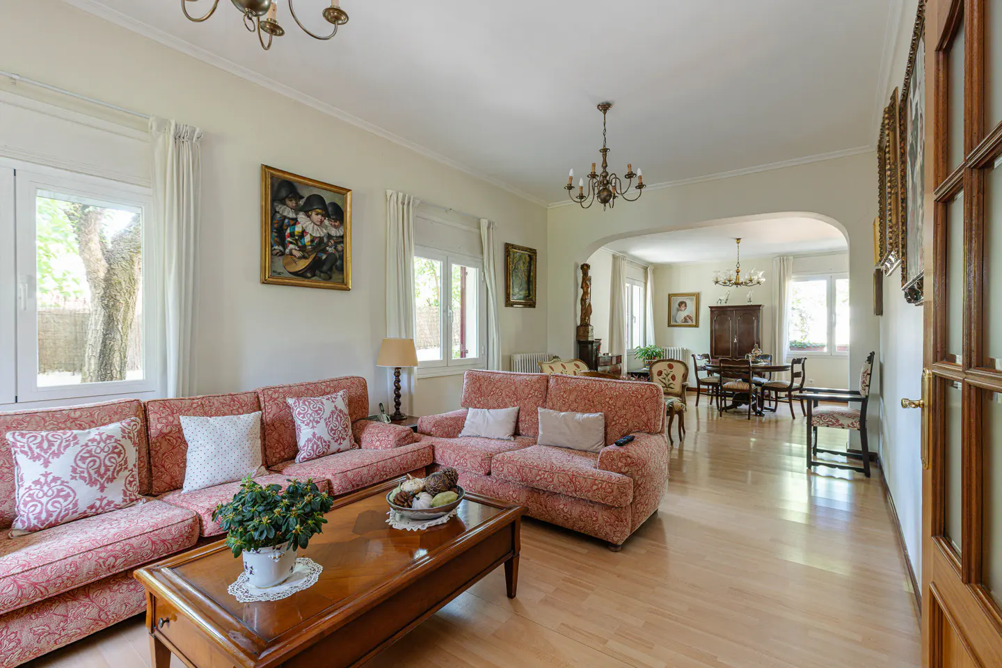 A bright living room with floral sofas, a wood coffee table, and a dining room in the background.