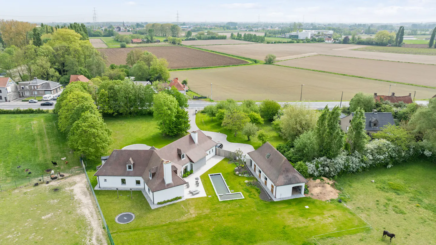 Aerial view of a white house with a brown roof, surrounded by green grass, trees, and farmland.