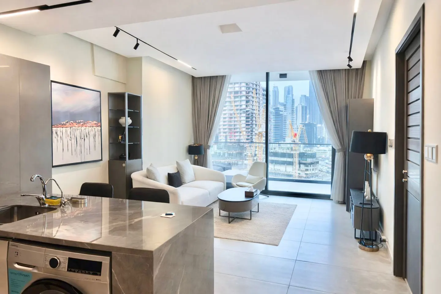 Modern apartment interior with a white sofa, city view, and gray kitchen island with a washing machine.
