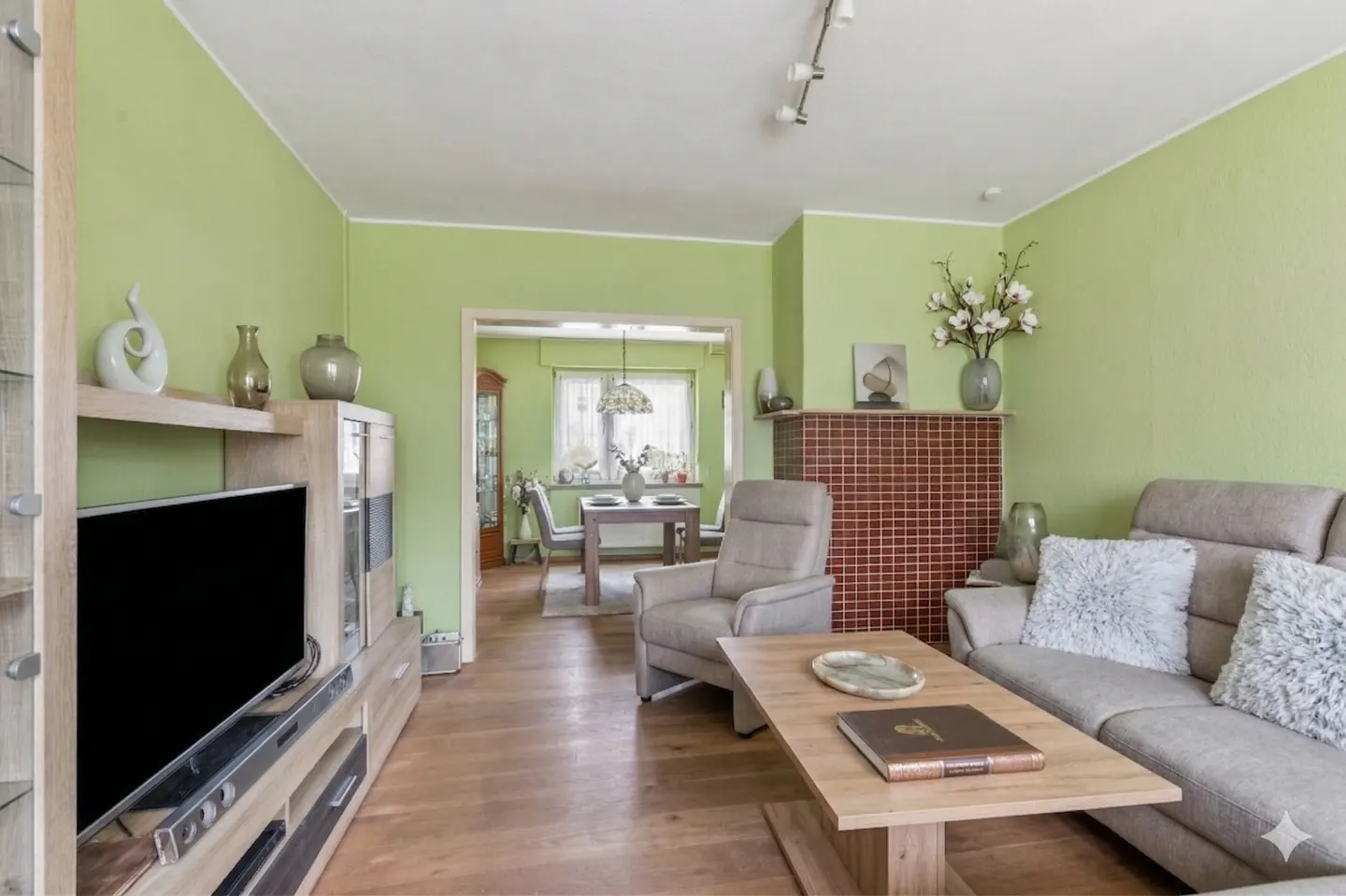 Living room with light green walls, wood floors, and furniture. A dining room is visible through an open doorway.